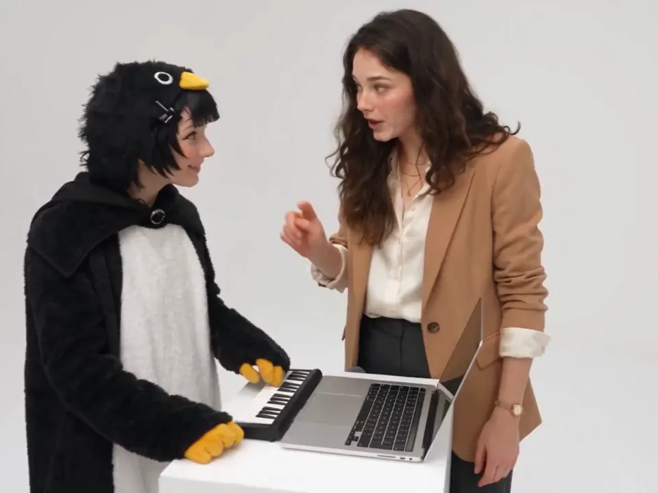 Two people at the laptop and mini keyboard, one directing with a pointed finger while the other plays